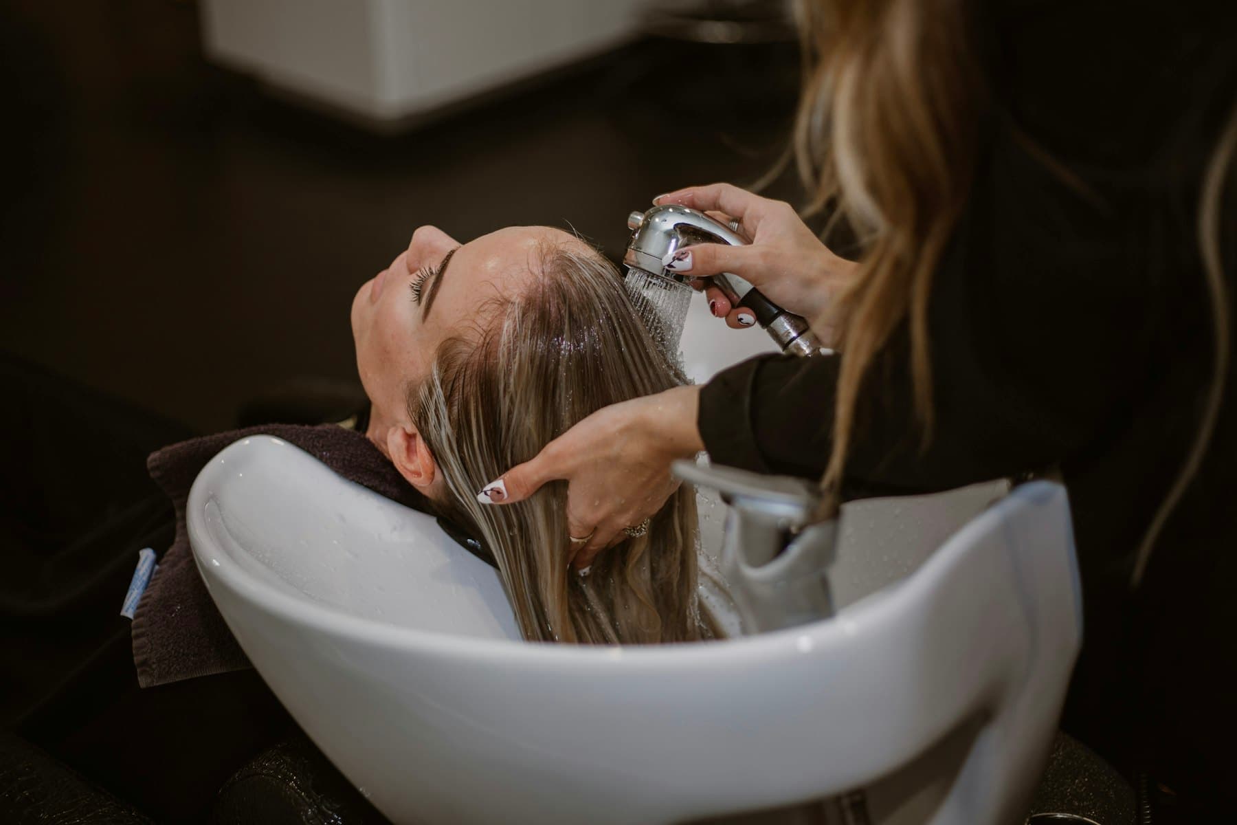 Client's hair being rinsed at a salon basin in low light