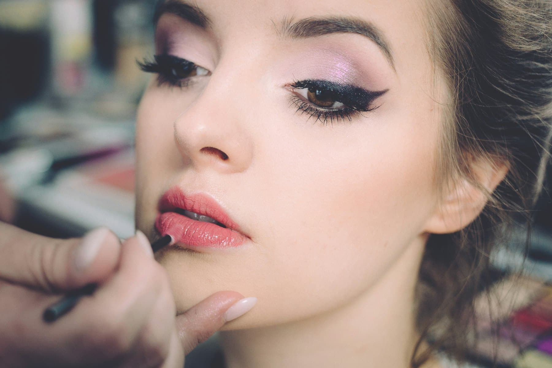 Makeup artist applying lipstick to a model with winged eyeliner