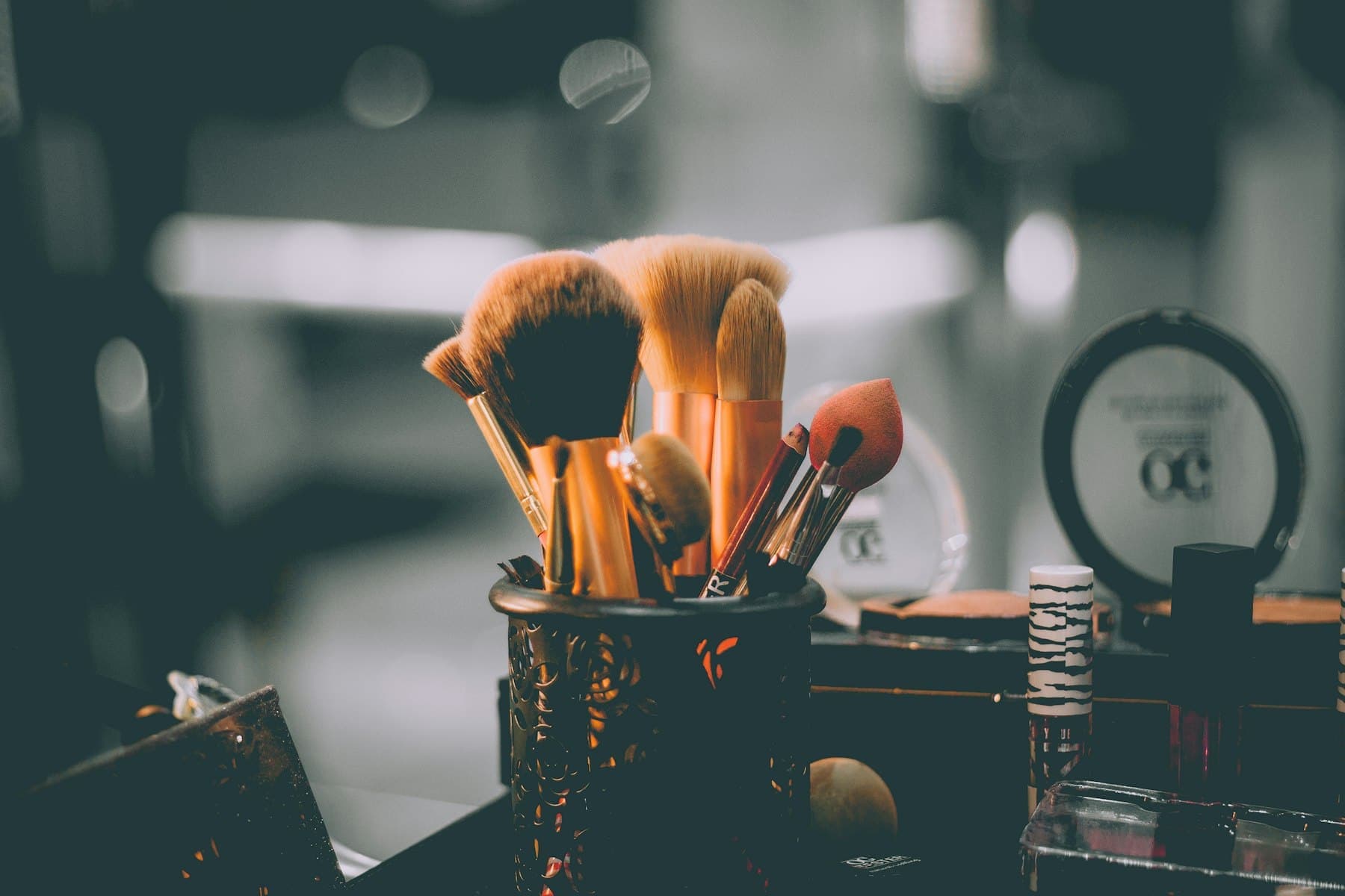 Makeup brushes in a cup on a dark dressing table