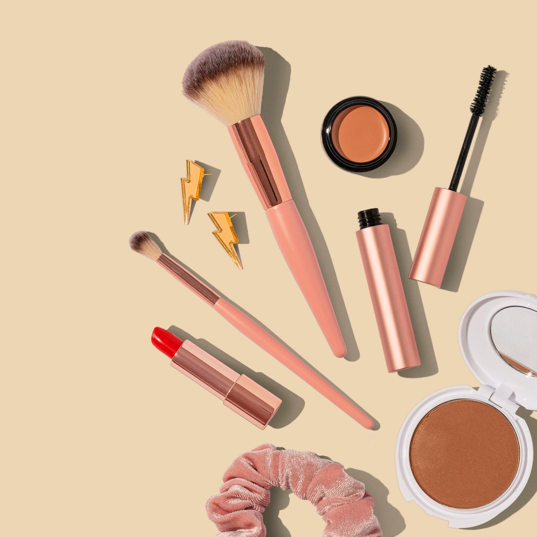 Rose-gold makeup brushes, lipstick and powder on a beige background