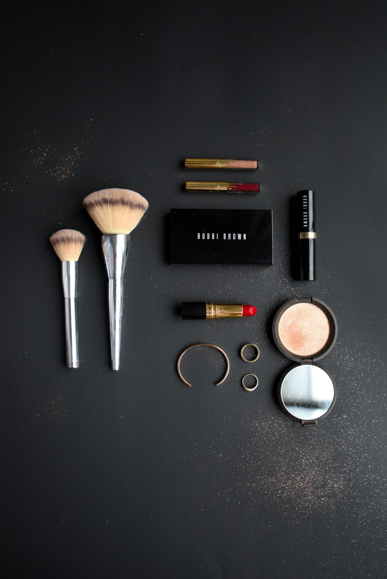 Makeup brushes, lipsticks and compact arranged on a black surface