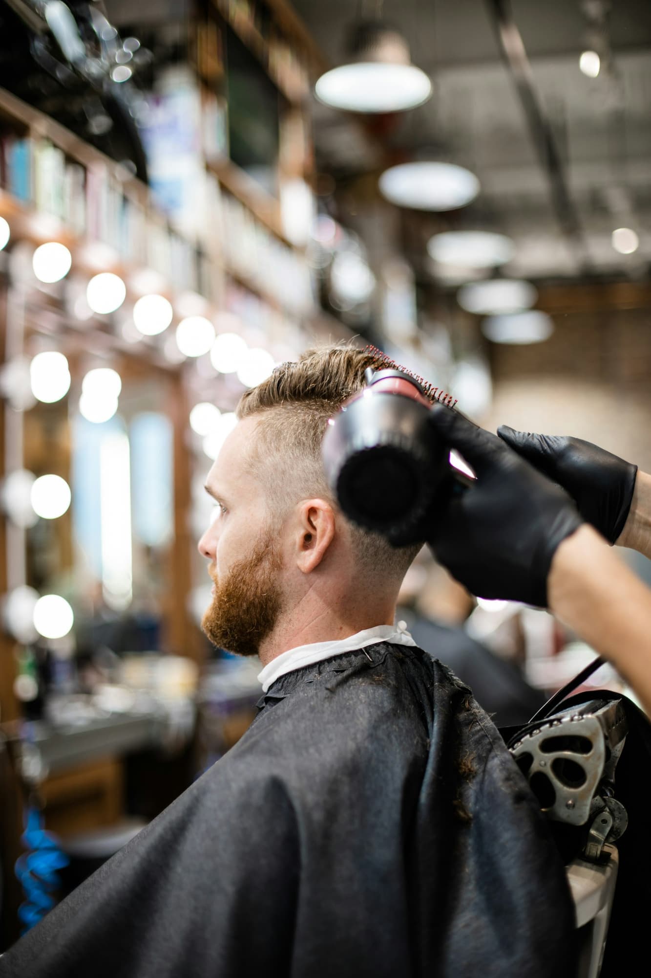Man with a beard having his hair blow-dried by a gloved barber