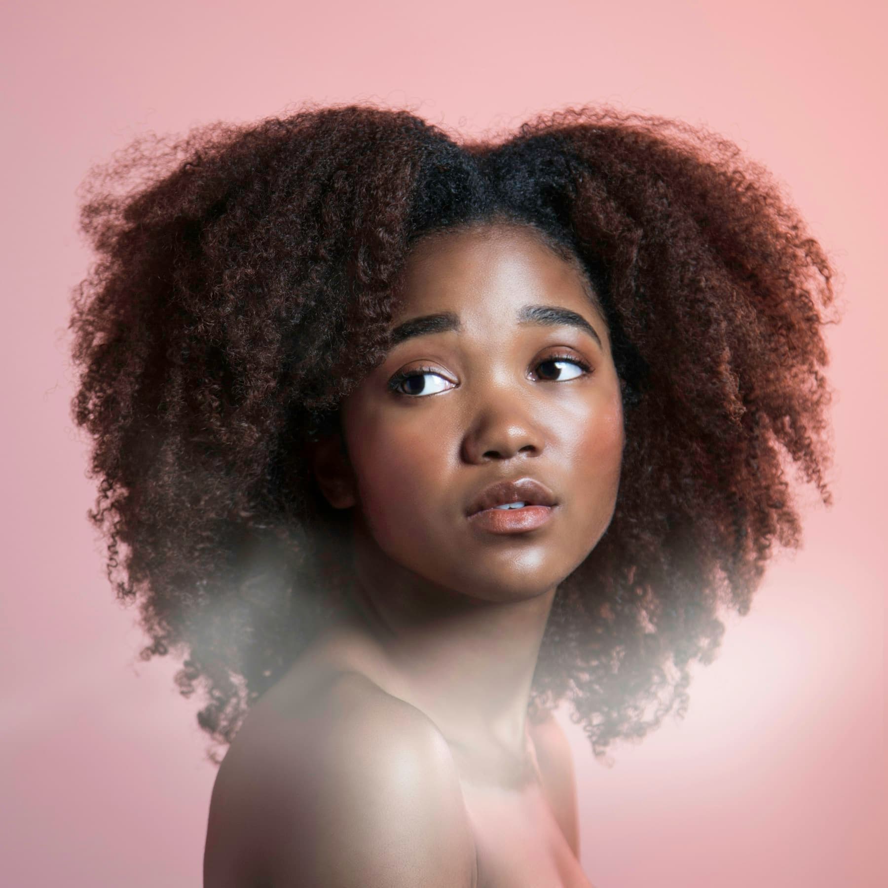 Portrait of a young woman with full natural curly hair against a pink background