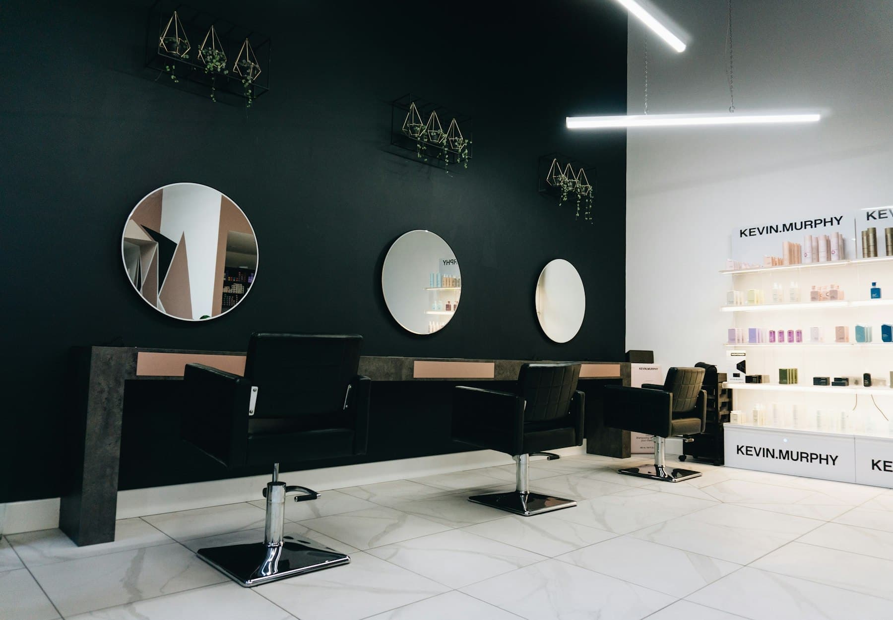 Minimal salon styling stations with round mirrors against a black wall