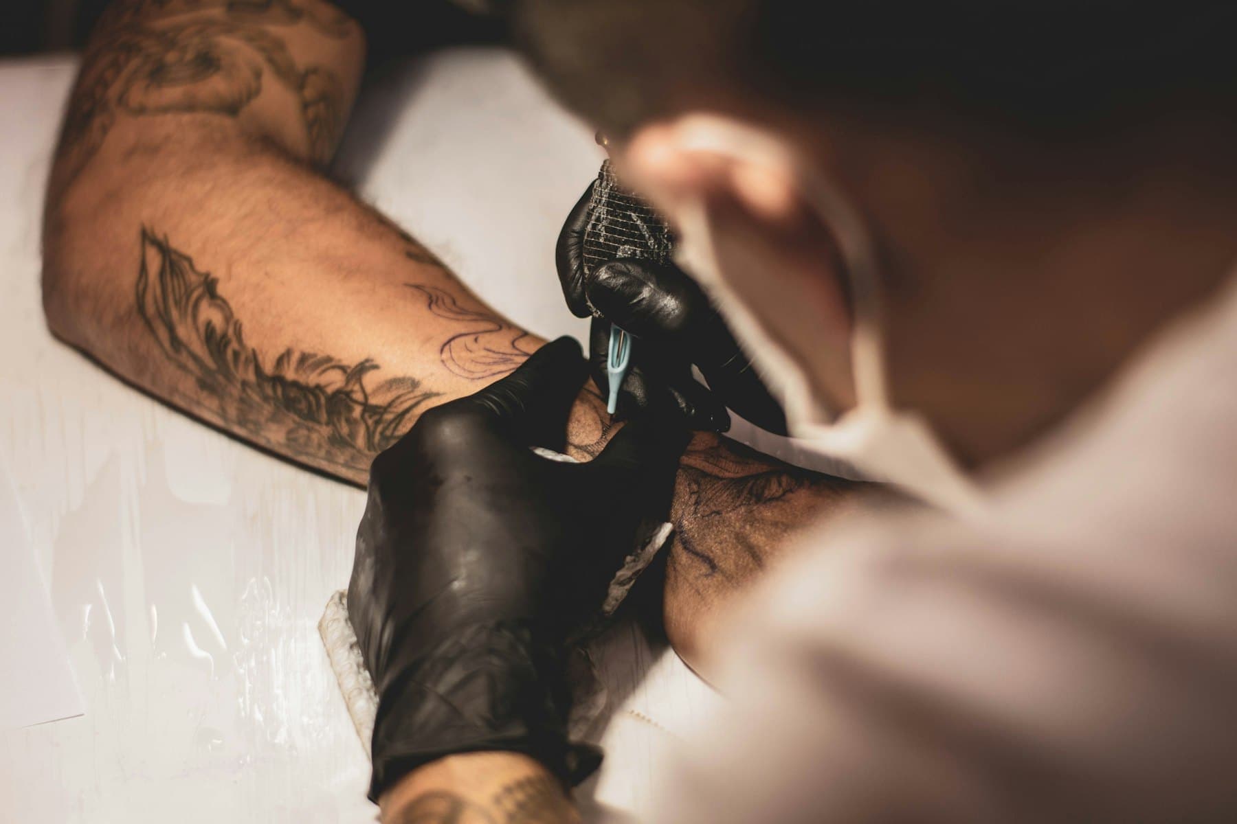 Gloved tattoo artist working on an arm tattoo