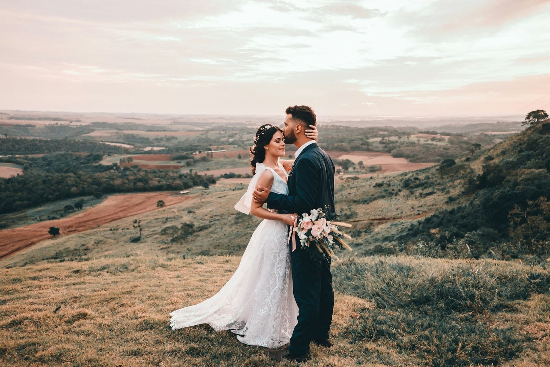Bride and groom embracing on a hillside at sunset