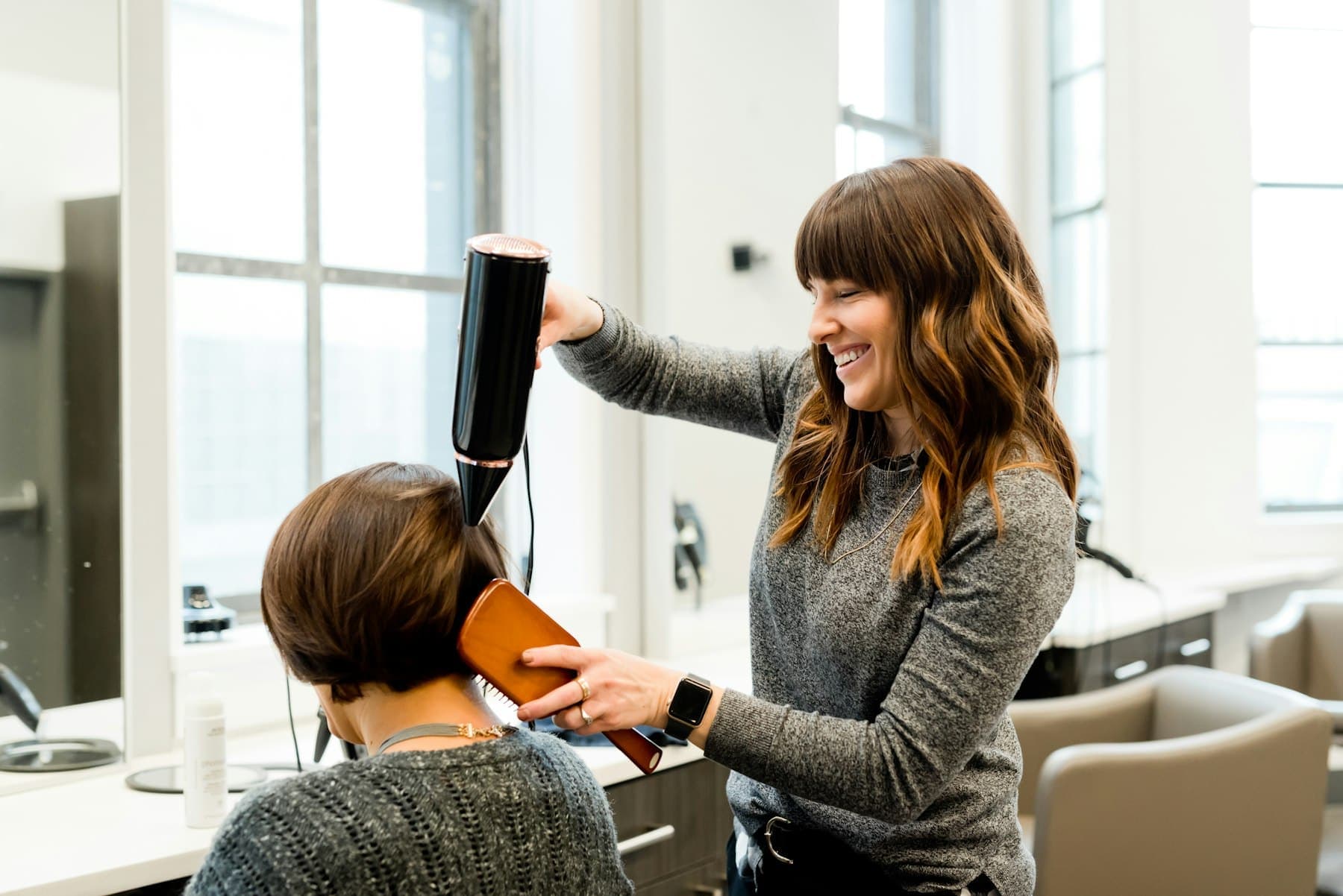 Stylist blow-drying a woman's short haircut in a bright salon
